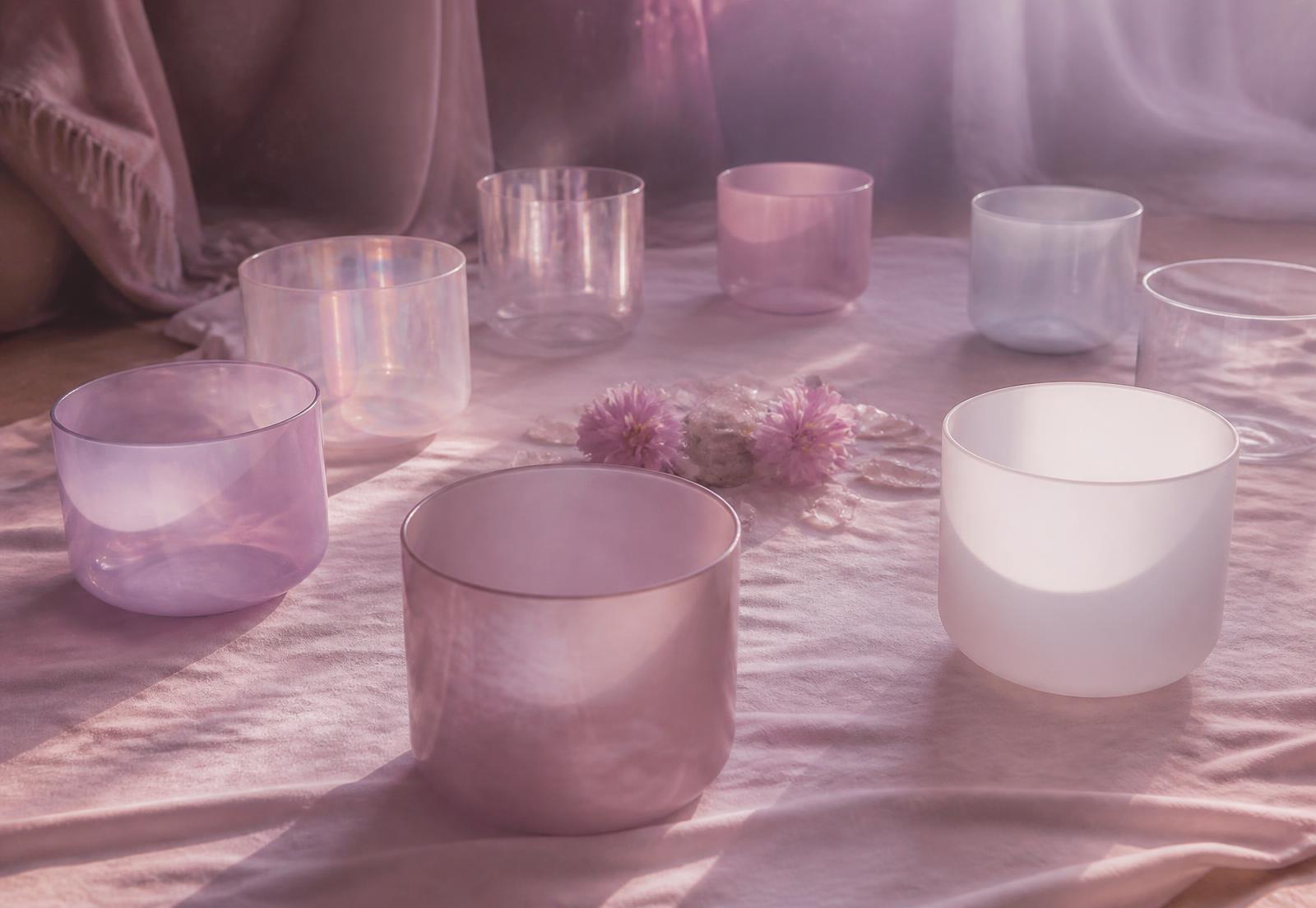 Crystal singing bowls arranged in a circle in soft pink light
